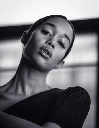 Striking black and white portrait of a young woman with glossy makeup, wearing a dark top, captured with a medium shot and eye-level angle.