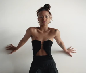 A woman wearing a black strapless top with a front cutout, posing against a white background with her arms out to her sides.
