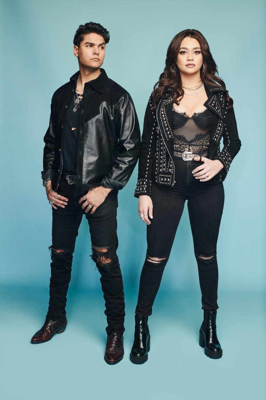 Full studio shot of a young adult couple in fashion-forward black and leather outfits against a light blue backdrop. Edgy style.