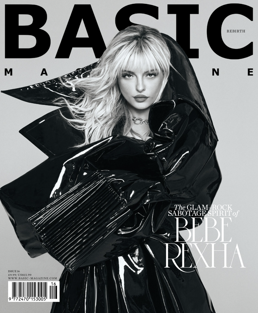 Magazine cover featuring Bebe Rexha in a black patent-leather hooded outfit. Her blond hair is styled with bangs. The background is grey.
