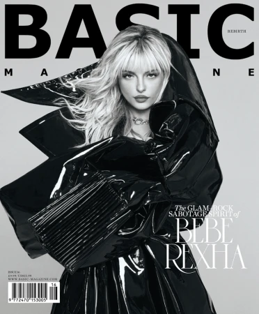 Magazine cover featuring Bebe Rexha in a black patent-leather hooded outfit. Her blond hair is styled with bangs. The background is grey.