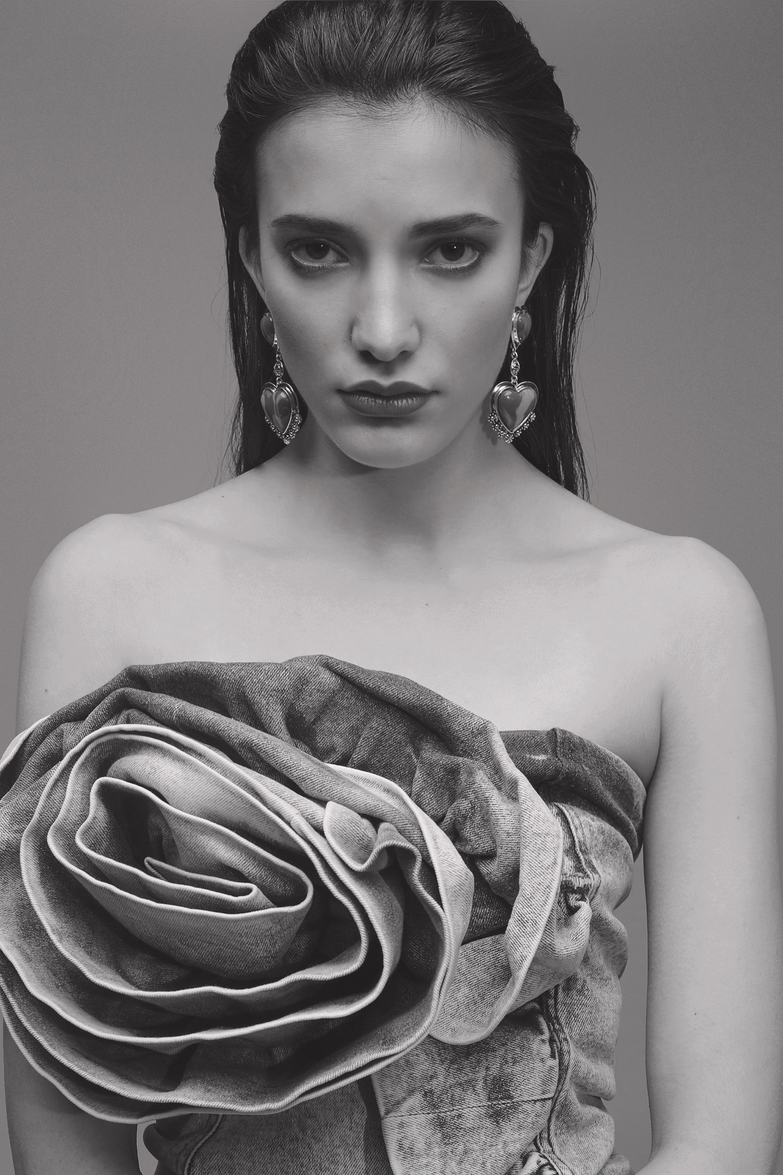 Black and white portrait of a woman with dark hair, wearing large heart earrings and a top designed as a denim rose.