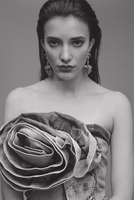 Black and white portrait of a woman with dark hair, wearing large heart earrings and a top designed as a denim rose.