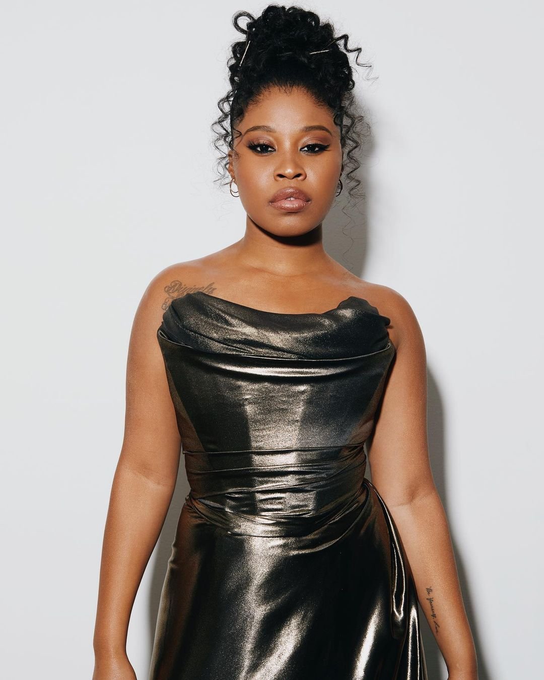 Black woman in a metallic strapless dress with hair in an updo against a white seamless background