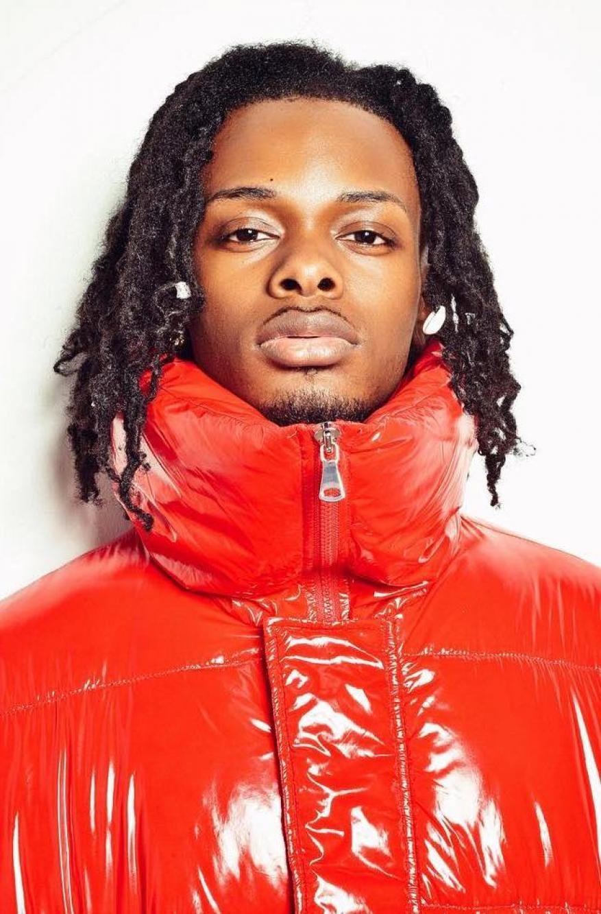 Portrait of a young adult male with dark hair wearing a puffy red jacket, shot in front of a neutral background, showcasing a fashion-forward look.