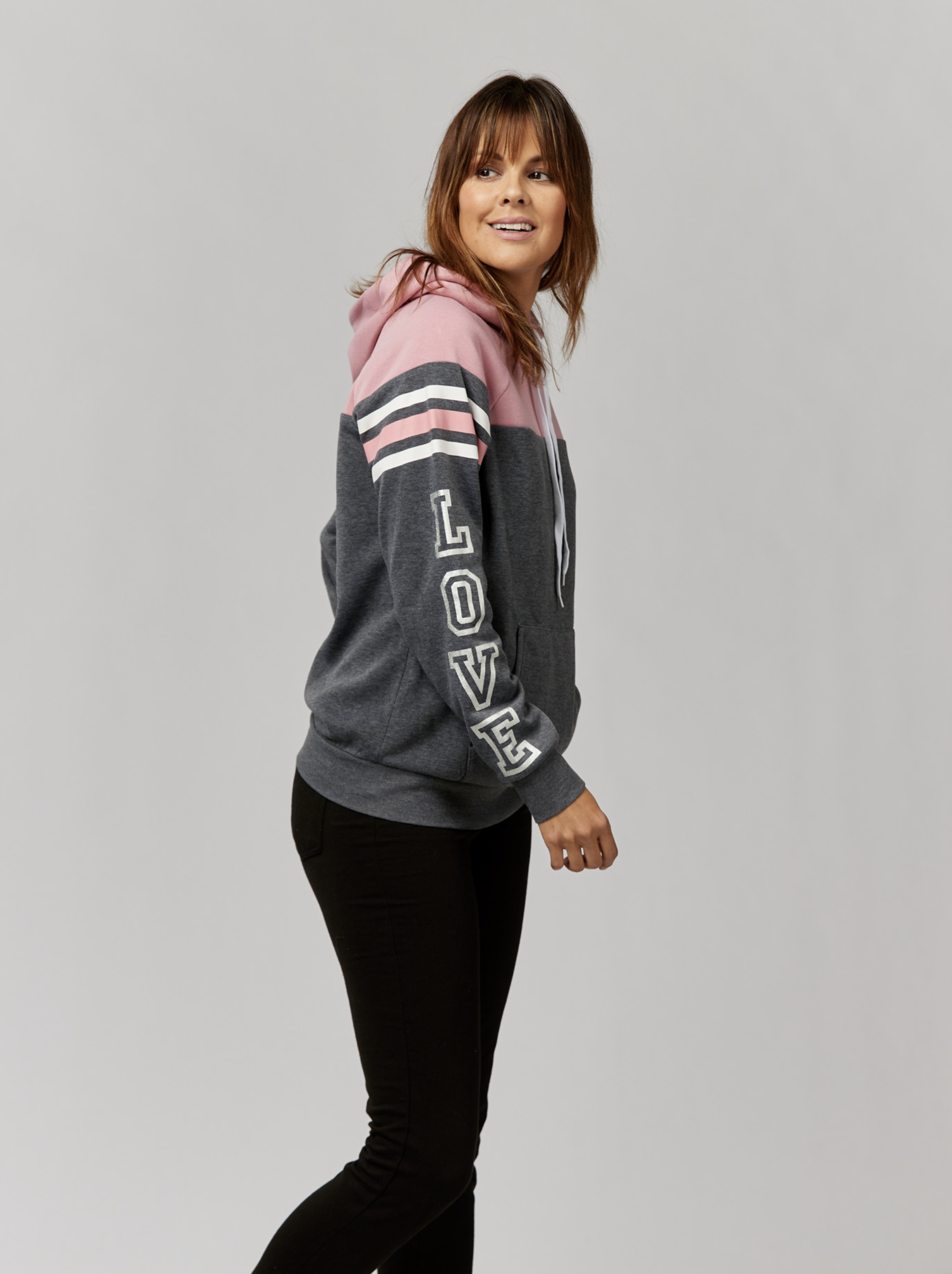 Attractive adult woman wearing a hooded sweatshirt with the word 'LOVE' printed on the sleeve poses in a studio setting.