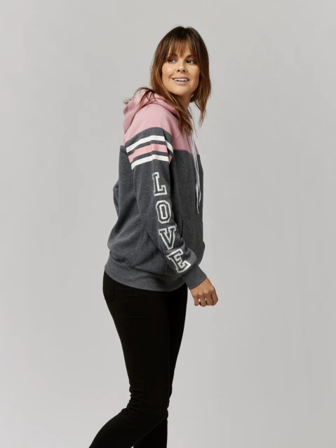 Attractive adult woman wearing a hooded sweatshirt with the word 'LOVE' printed on the sleeve poses in a studio setting.