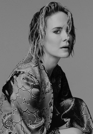 Monochrome portrait of an adult woman with wet, short blonde hair wearing a patterned silk robe against a plain gray backdrop.