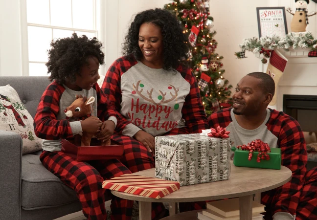 Family in matching pajamas sit by a Christmas tree unwrapping gifts, creating a warm, festive, holiday celebration scene together.