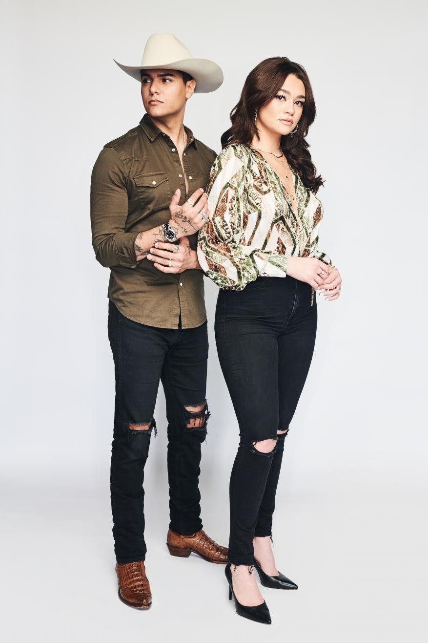 Man in cowboy hat and woman in patterned blouse standing against a white seamless background