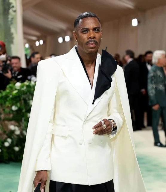 Elegant man in a white suit with cape detail at a formal event, showcasing stylish attire and posing for a portrait.