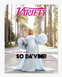 Da'Vine Joy Randolph holding an Oscar statue wearing a light blue sequin gown with feathered sleeves on a palm tree-lined street