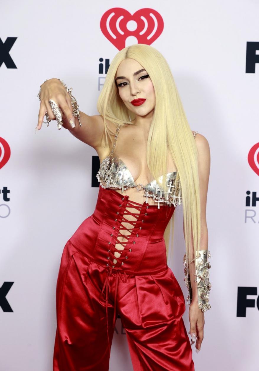 Blonde woman with red corset top and silky red pants poses in front of iHeartRadio backdrop at a red carpet event.