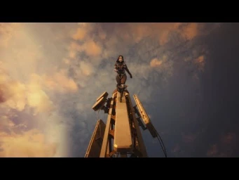 A woman in intricate black costume design standing on top of a narrow tower structure against a cloudy sunset sky.