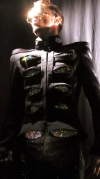 Man wearing a dark jacket with rhinestone-embellished cutouts and sunglasses catching a bright glare.