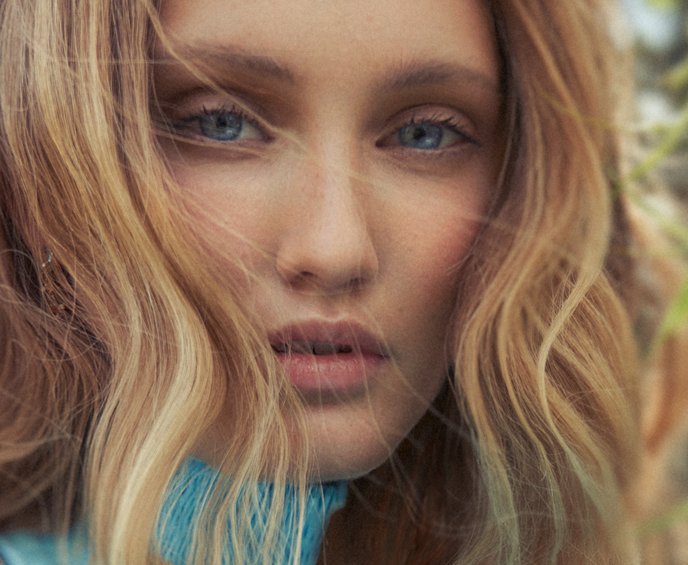Close-up portrait of a young adult woman with light blonde hair and blue eyes, looking directly at the camera with a neutral expression.