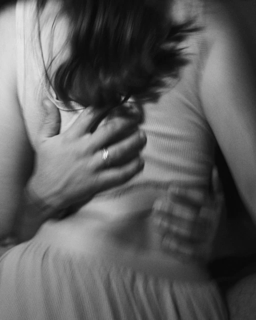 Monochromatic image of a man embracing a woman from behind, focusing on their midsections and the intimate connection between them.