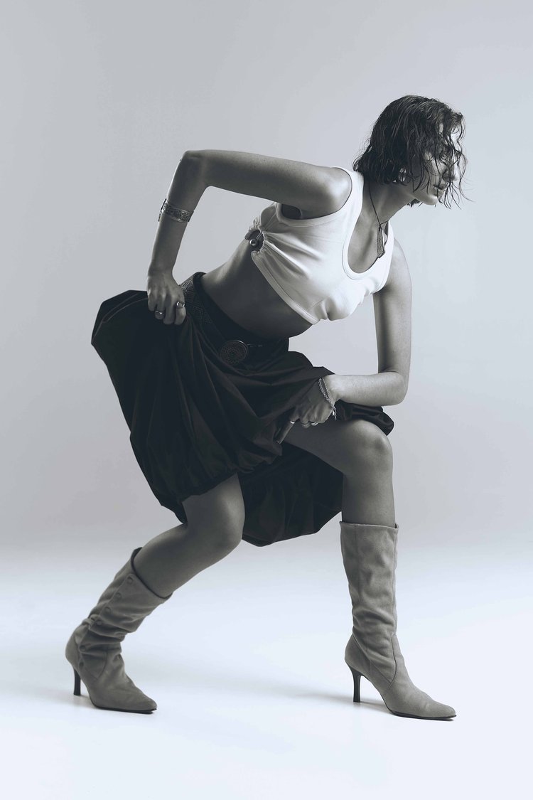 Woman in motion wearing boots and a skirt in a studio setting, captured with a shallow depth of field and cool monochrome tones.