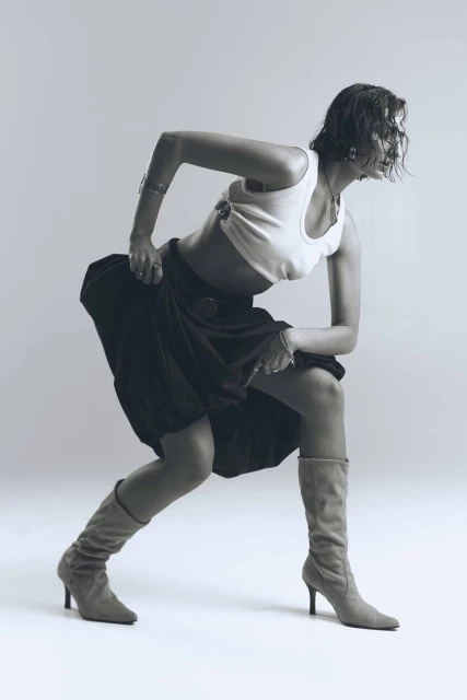 Woman in motion wearing boots and a skirt in a studio setting, captured with a shallow depth of field and cool monochrome tones.