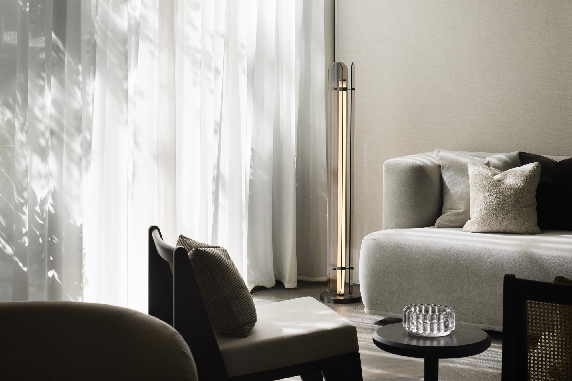Contemporary living room with modern floor lamp, light grey sofa, and accent chairs bathed in soft natural light through sheer curtains.