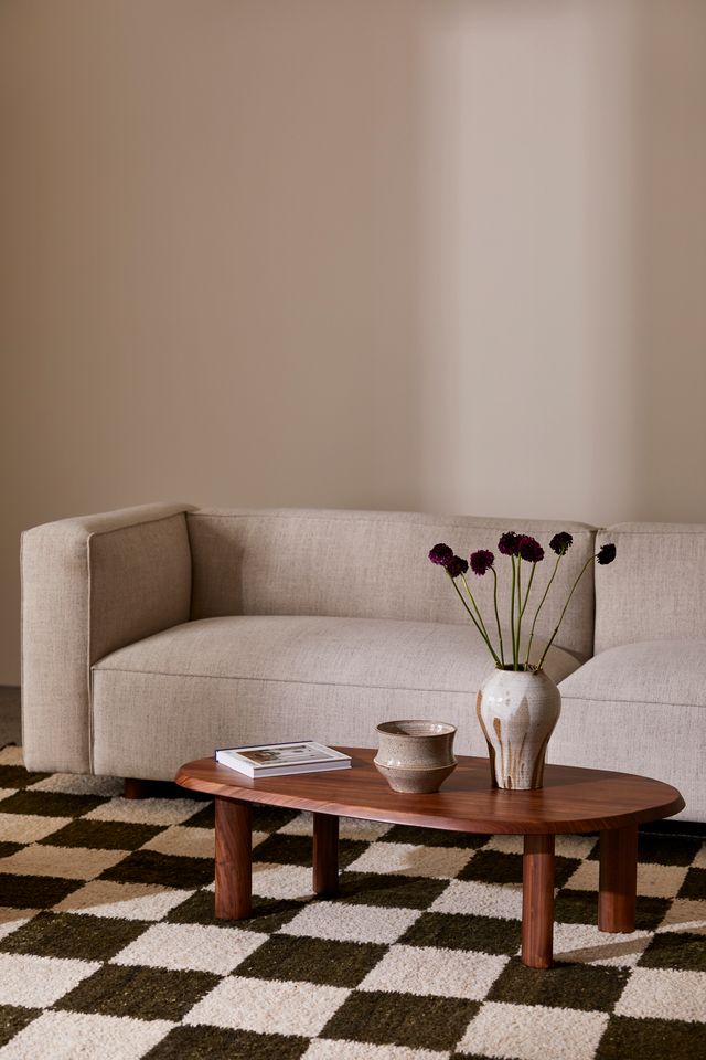 Living room interior: beige sofa, wooden coffee table with flowers and ceramic vases, checkered rug, soft, neutral color palette.