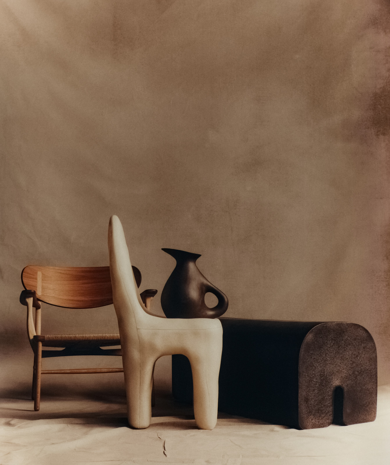 Still life photograph featuring an arrangement of furniture and decorative objects in muted earth tones against a textured backdrop.