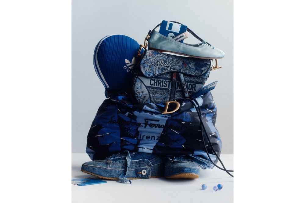 Still life fashion studio shot of a blue Gucci hat, Christian Dior purse, Miu Miu shoe, Salvatorre Ferragamo jacket and denim shoe.