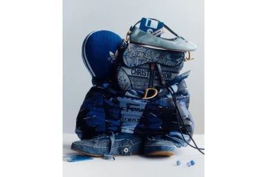 A towering stack of blue designer fashion items including handbags, footwear, and accessories on white backdrop
