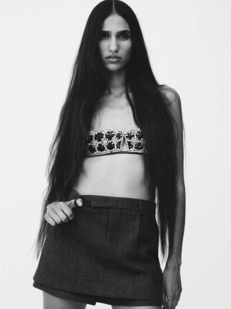 Portrait of a woman with long dark hair wearing a patterned strapless top and dark skirt against a white background