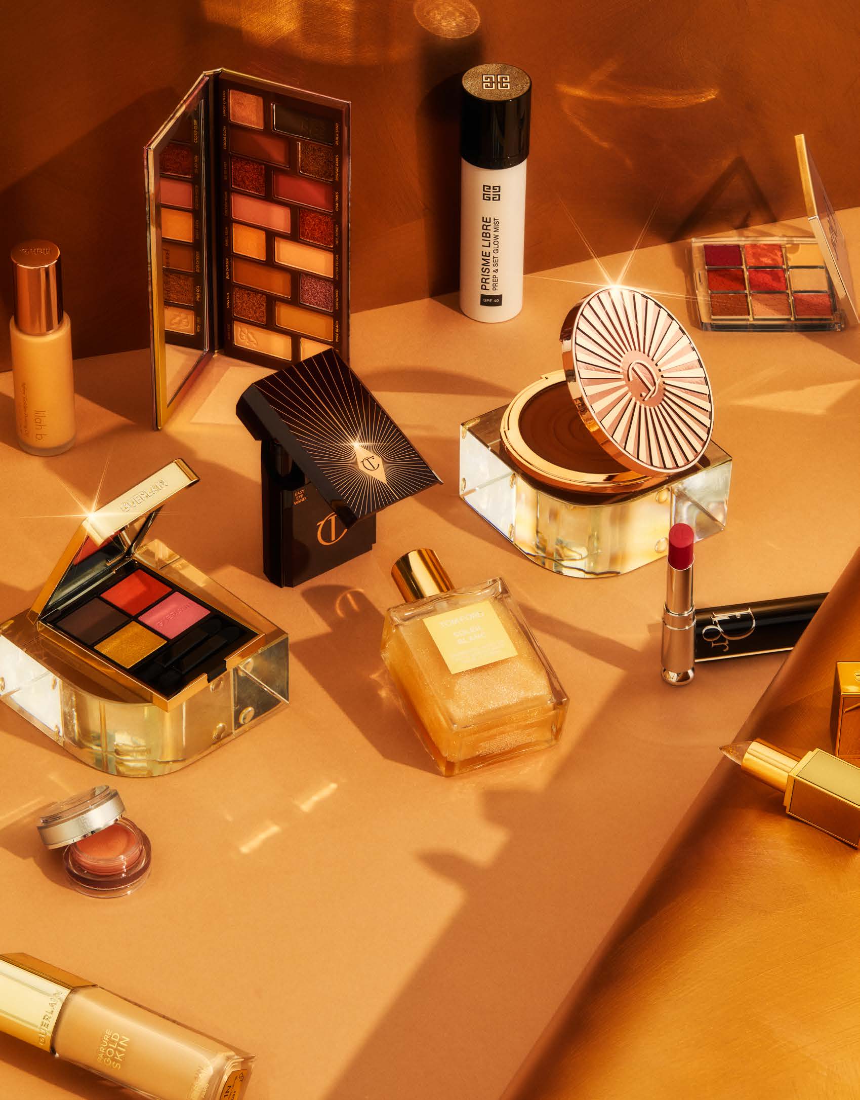 Beauty still life showcasing a variety of luxury cosmetic products in gold and neutral tones, including eyeshadow palettes, foundation, and lipstick.