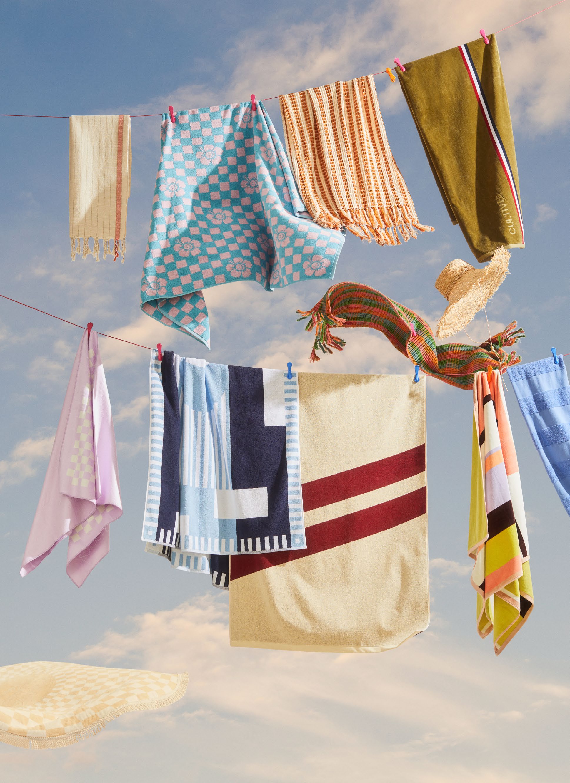 Various colorful towels and textiles hang on a clothesline against a partly cloudy sky, suggesting a breezy, outdoor setting.