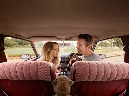 Man and woman sitting inside a vintage car looking at each other with a dog in the foreground