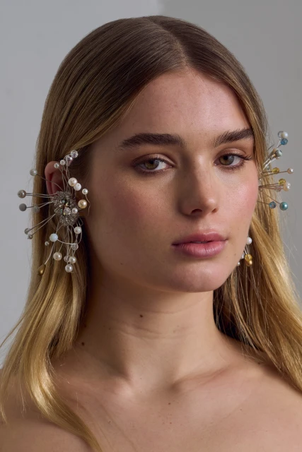 Close-up portrait of a fair-skinned woman with fair hair and elaborate ear jewelry against a neutral background in soft, diffused light.