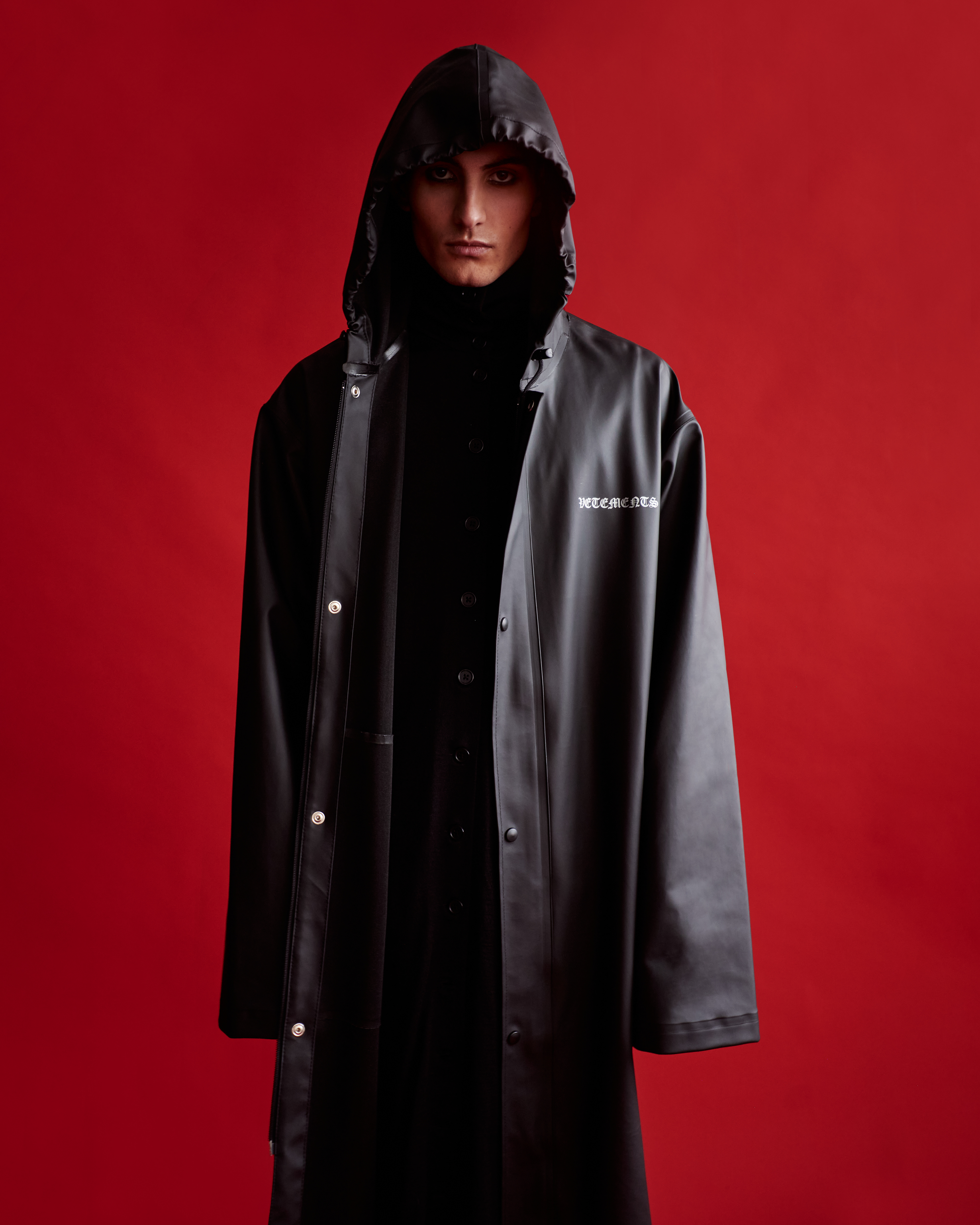 Model in a black hooded coat against a vibrant solid red background with dramatic makeup by Jack Chesher