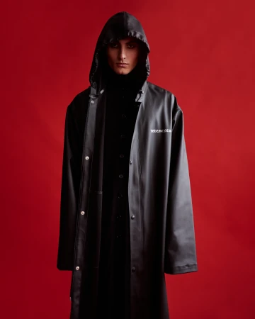 Model in a black hooded coat against a vibrant solid red background with dramatic makeup by Jack Chesher