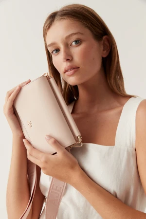 Close-up portrait of a woman holding a light pink leather crossbody bag against a plain white studio background.