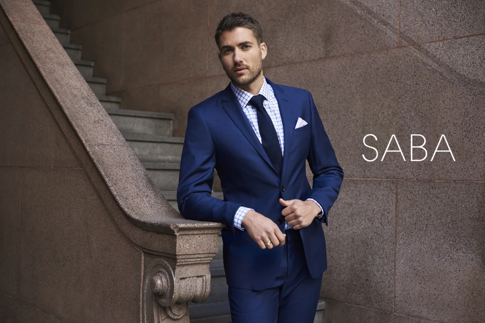 Fashion shoot of a man in a blue suit leaning against a marble staircase with a neutral stone wall, showcasing a stylish and professional look.