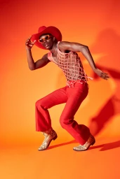 Black man in a red cowboy hat and trousers dancing against an orange background styled by Josie McManus