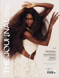 Black woman with long voluminous hair wearing cream cutout top against a plain light background