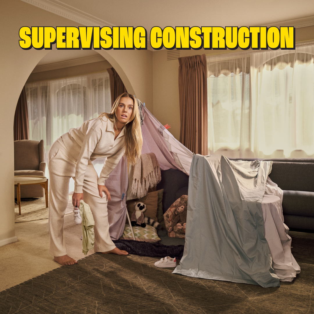 A woman in pajamas pretends to supervise a blanket fort construction project in her home living room, creating a humorous moment.