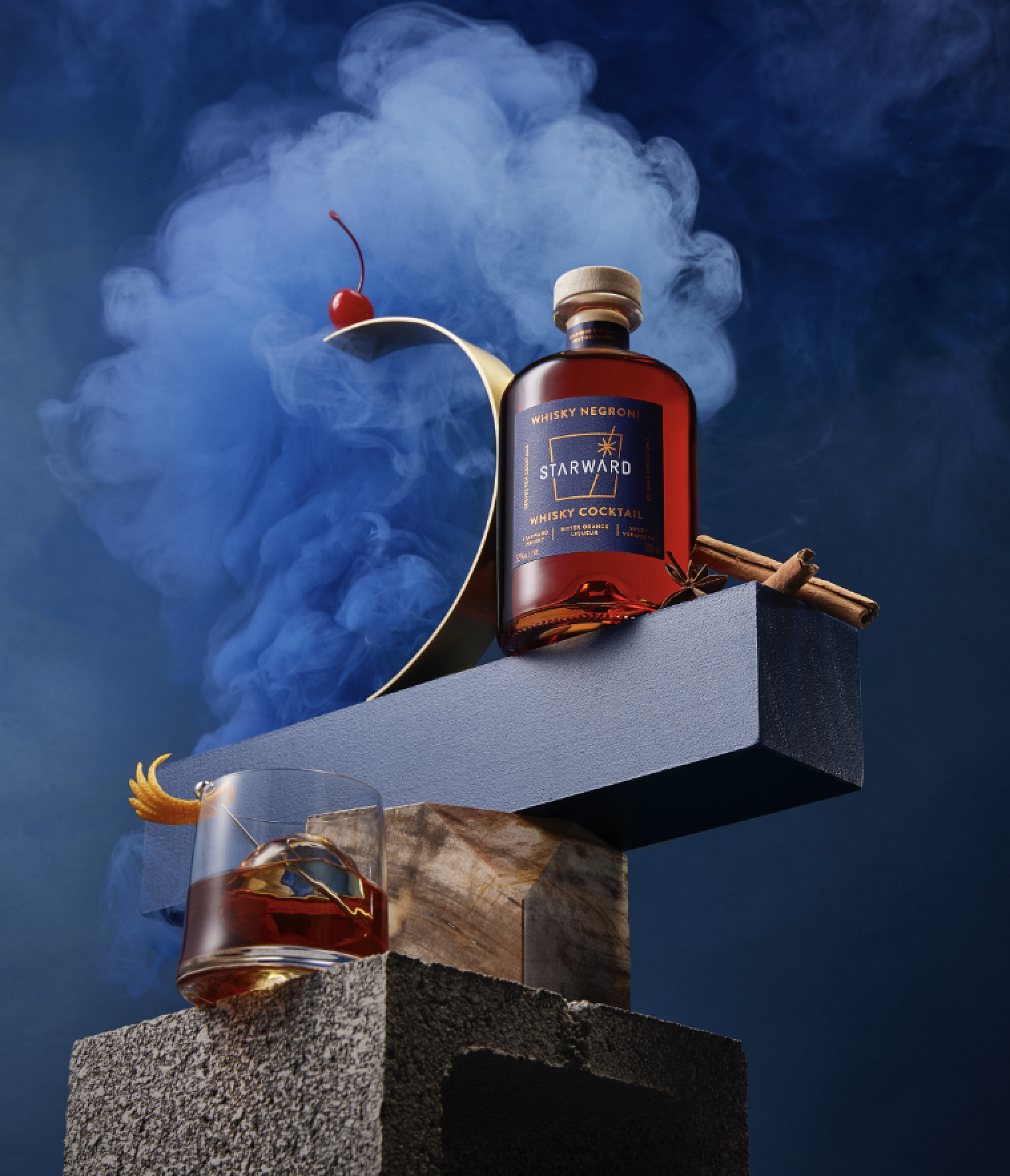 Whiskey Negroni cocktail in a bottle, glass with orange peel, and cherry, staged on a stone block with smokey blue background.