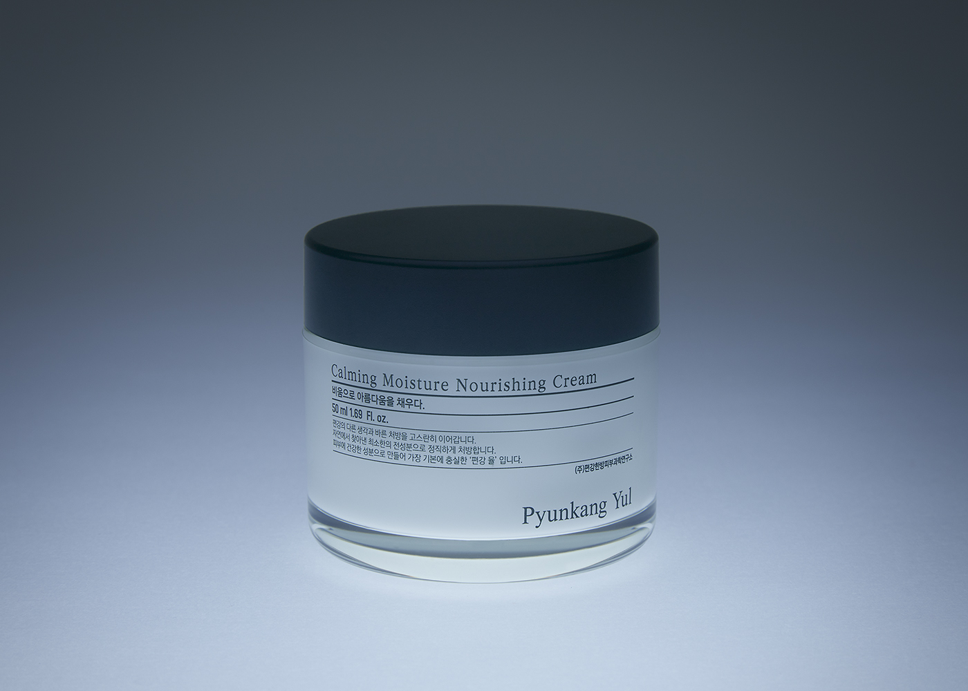 Cosmetic cream jar close-up. White jar with dark lid, label with 'Calming Moisture Nourishing Cream' text, beauty product, studio shot.