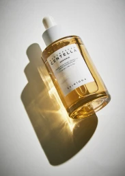 Amber glass skincare dropper bottle casting a warm golden shadow on a white studio background.