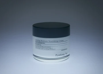Pyunkang Yul Calming Moisture Nourishing Cream jar centered on a cool blue-grey vignette studio background.