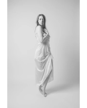 Monochrome portrait of a woman in a long slip dress standing against a plain backdrop by Paul G Dodd Photography