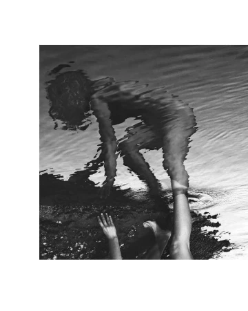 Monochrome shot of a woman crouched at the water's edge, her reflection distorted by ripples, creating an abstract and artistic effect.