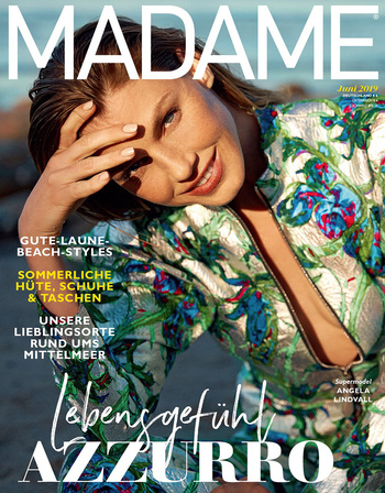 Magazine cover featuring a woman with floral top, smiling with hand on her head, against a backdrop of greenery and a hint of the sea.
