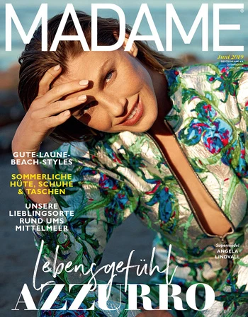 Magazine cover featuring a woman with floral top, smiling with hand on her head, against a backdrop of greenery and a hint of the sea.