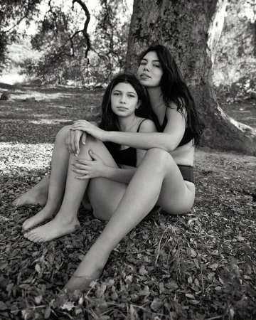 Two women seated together at the base of a large tree outdoors in a black and white portrait by Sylve Colless.