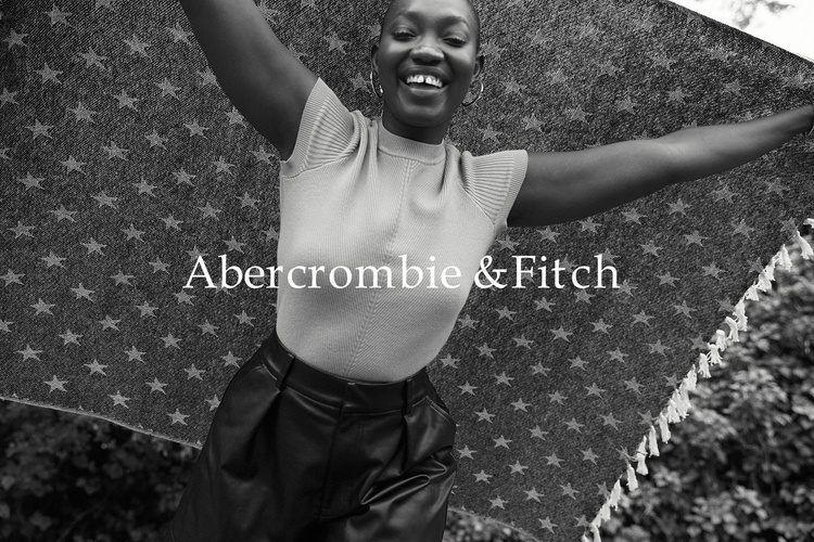 Smiling African-American woman outdoors, holding a patterned blanket in a fashion shot for Abercrombie & Fitch with a monochrome aesthetic.